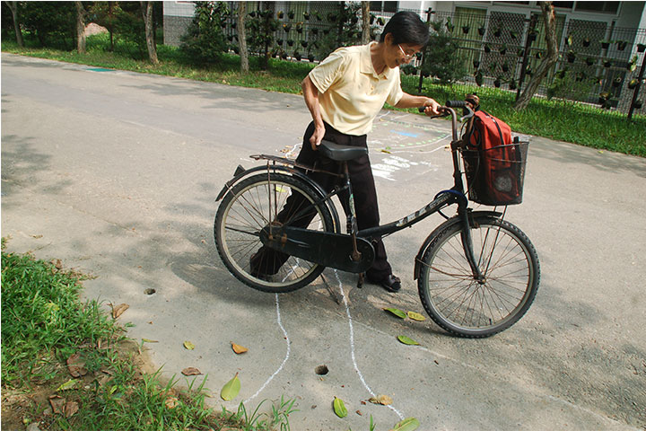 一位老師正小心翼翼地把腳踏車抬過螞蟻專用道，深怕一不留神便傷害了一個生命。