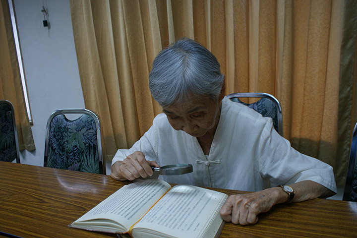 83歲的福智學員周妙蓉，讀經論時，須要用大字版的經論加放大鏡才看得到字。儘管如此，她仍很開心、有樂趣地學習，一點也不受雙眼可能失明的病障影響。
